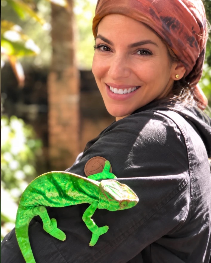 Our founder smiling over her shoulder with a green chameleon on her arm